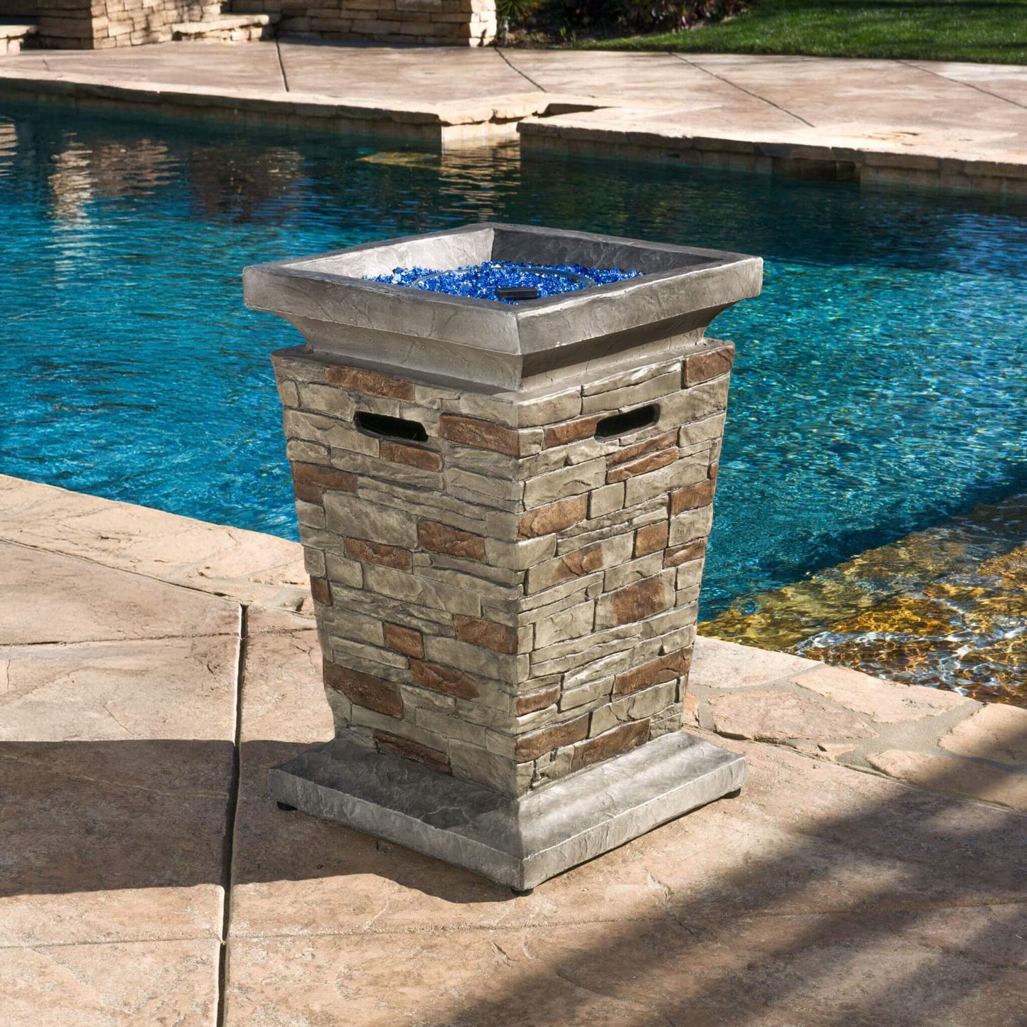 Decorative stone fire pit with blue glass stones by a pool