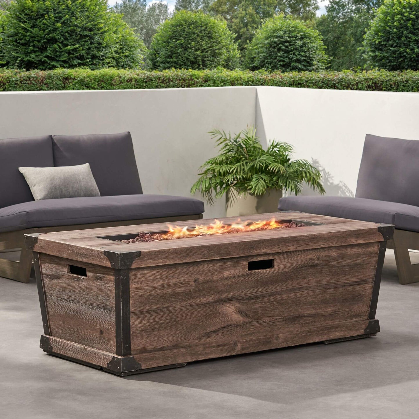Wooden fire pit table with flames on a patio with outdoor furniture and plants.