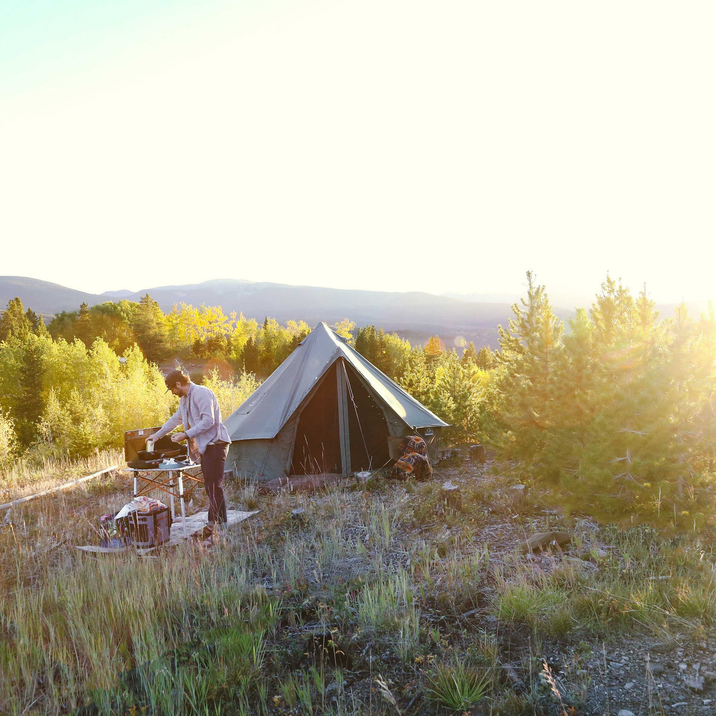 Person setting up a tent in a scenic outdoor setting with trees and mountains.