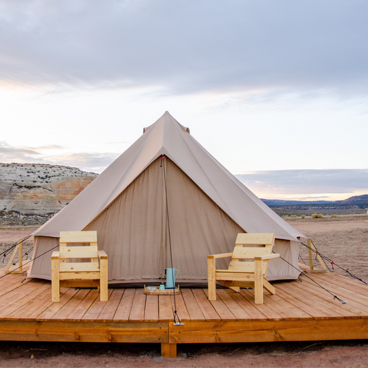 Beige tent with wooden deck and chairs in a desert landscape