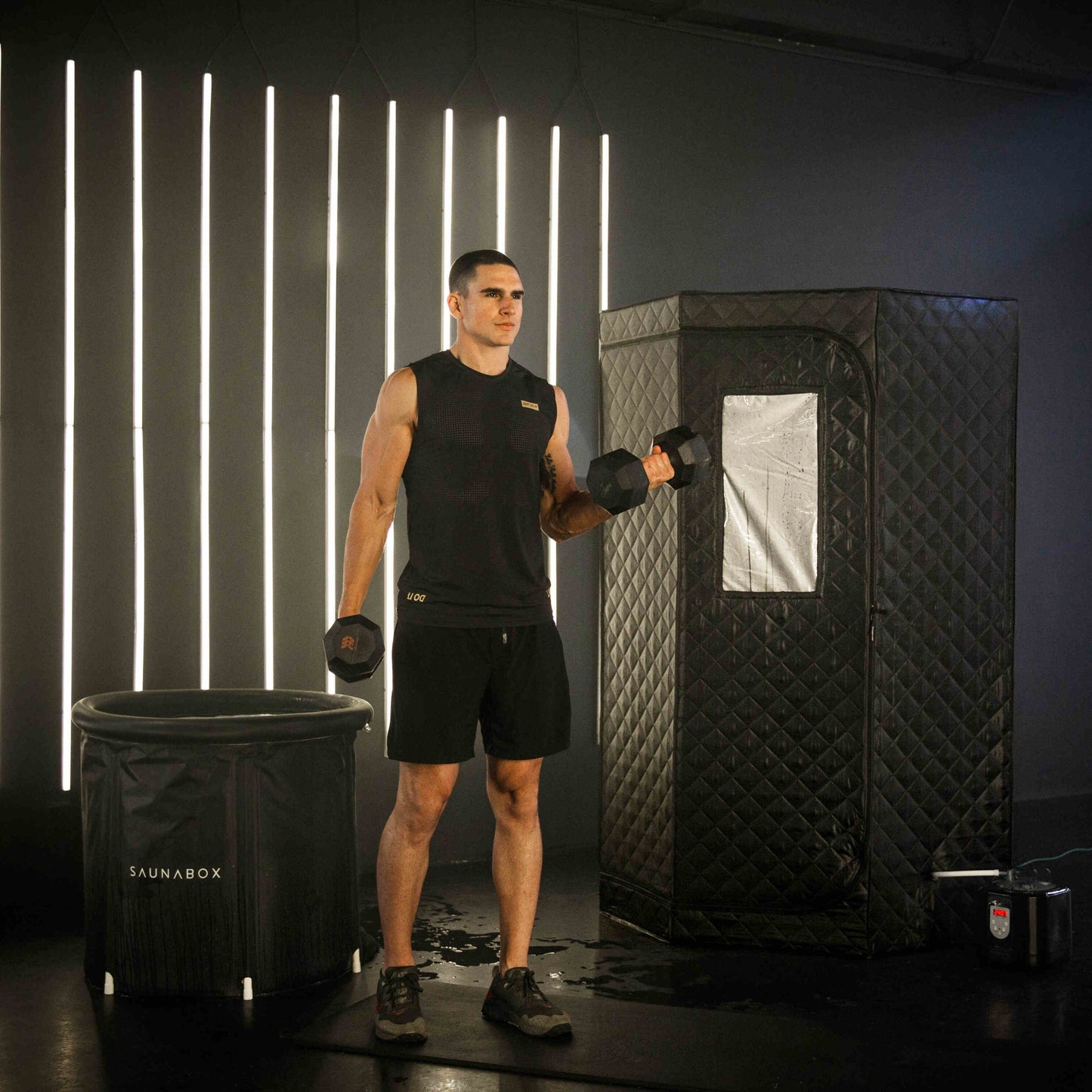 Man holding dumbbells in front of a black sauna box with illuminated vertical lights on the wall.