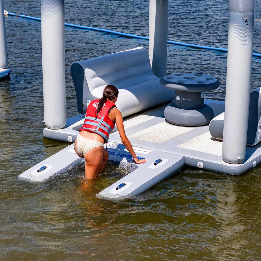 Users climbing onto the Aquaglide Swimstep XL, a low-profile boarding platform, in a lake aquapark setup