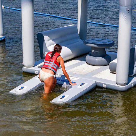 Users climbing onto the Aquaglide Swimstep XL, a low-profile boarding platform, in a lake aquapark setup