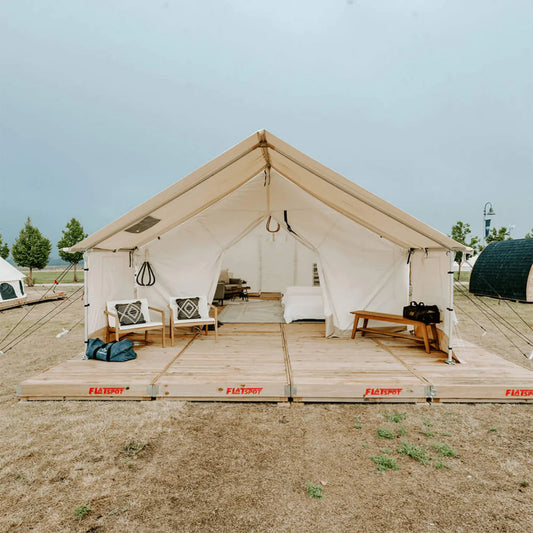 Large beige tent with wooden platform and furniture in a camping setting
