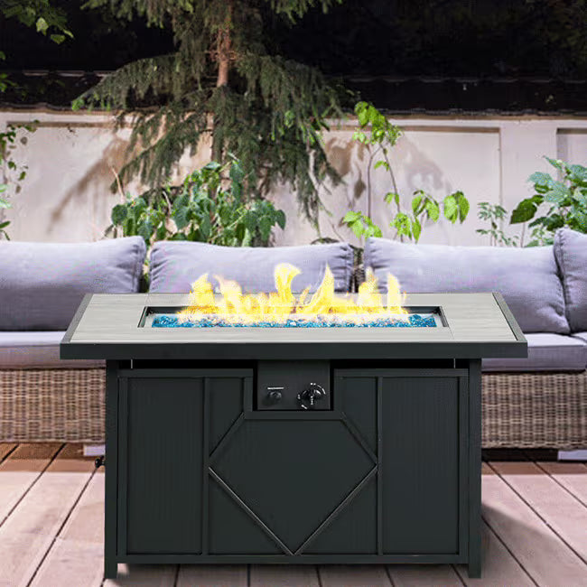 Outdoor fire pit table with flames on a patio with a couch and plants in the background