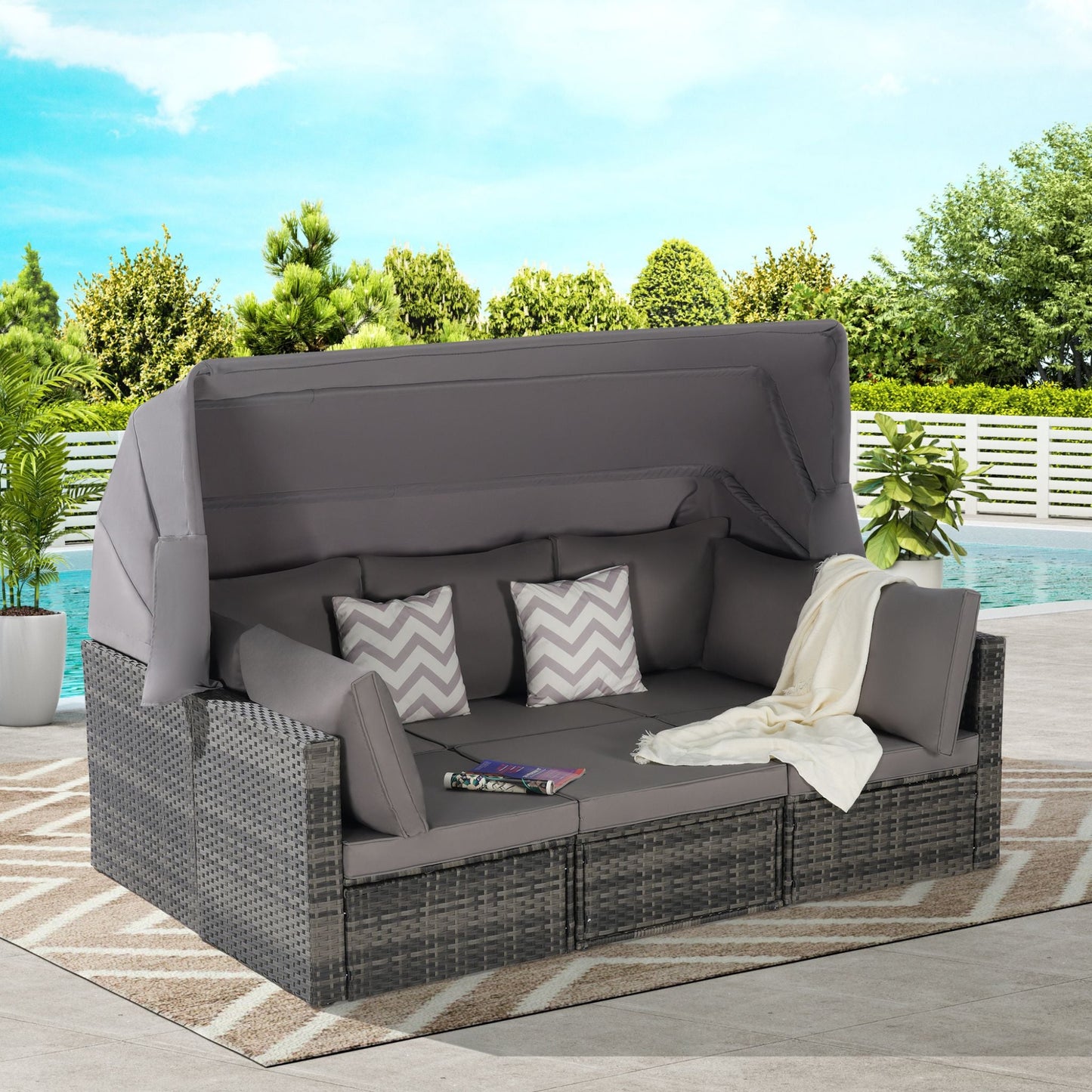 Outdoor patio sectional with cushions and a blanket on a patio with pool and trees in the background