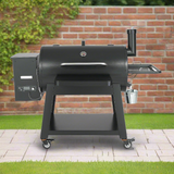 Black barbecue grill on wheels with a brick wall and greenery in the background