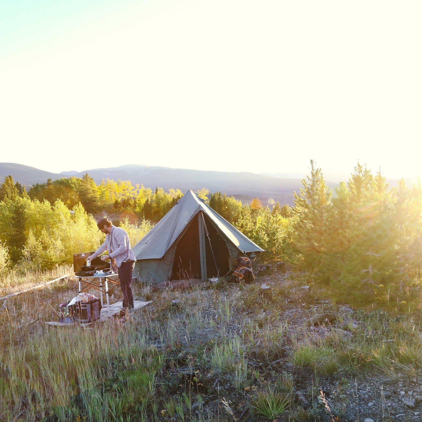 Person setting up a tent in a scenic outdoor setting with trees and mountains.