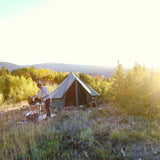 Person setting up a tent in a scenic outdoor setting with trees and mountains.