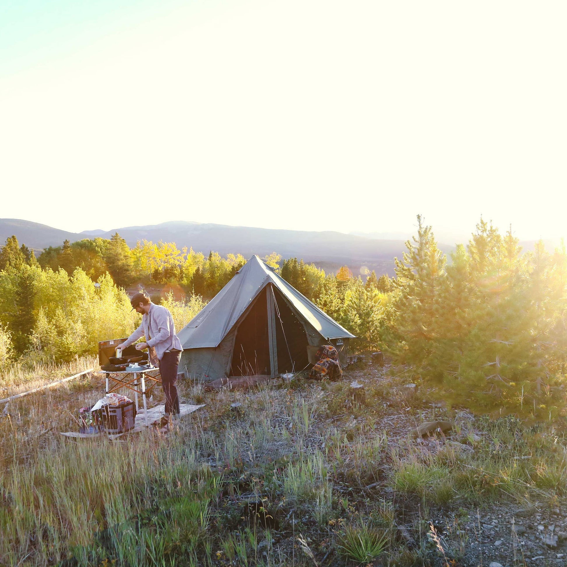 Person setting up a tent in a scenic outdoor setting with trees and mountains.