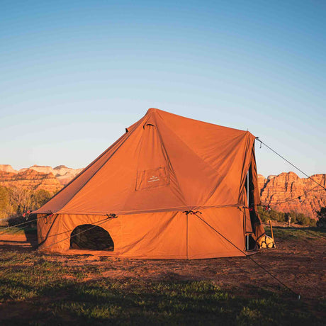 Brown tent set up in a field with mountains in the background