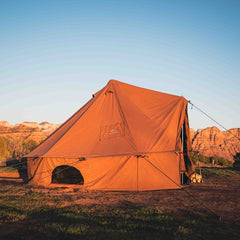 Brown tent set up in a field with mountains in the background