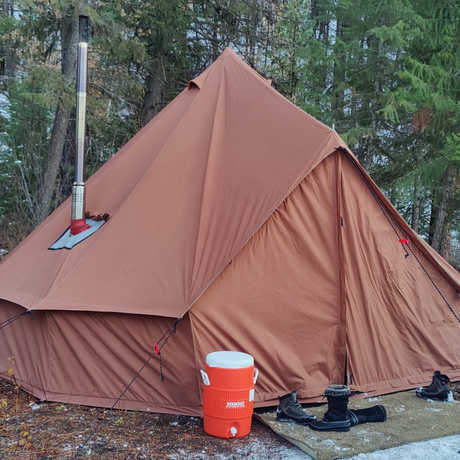 Brown tent with a chimney and orange cooler in a forest setting