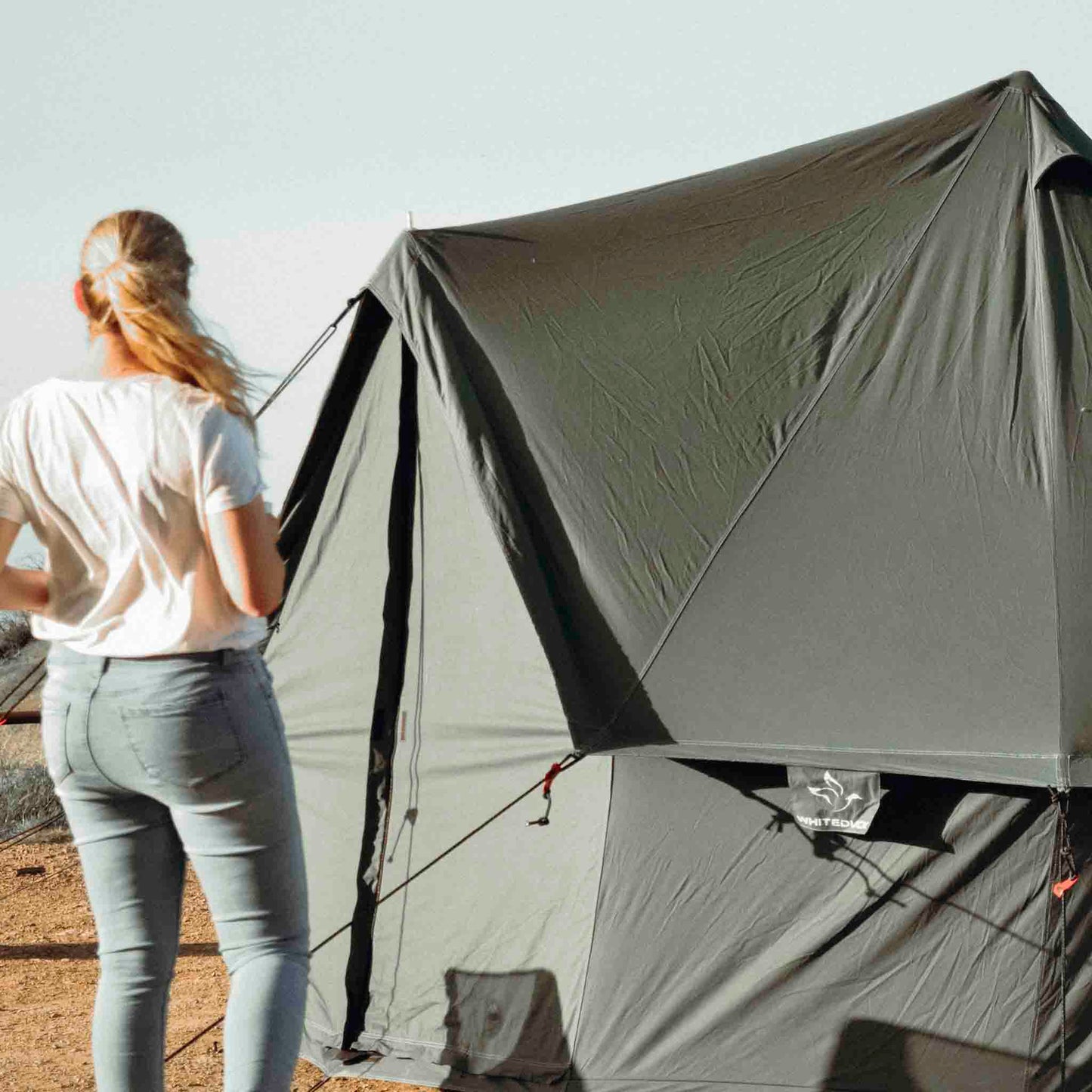 Person standing next to a large green tent in an outdoor setting