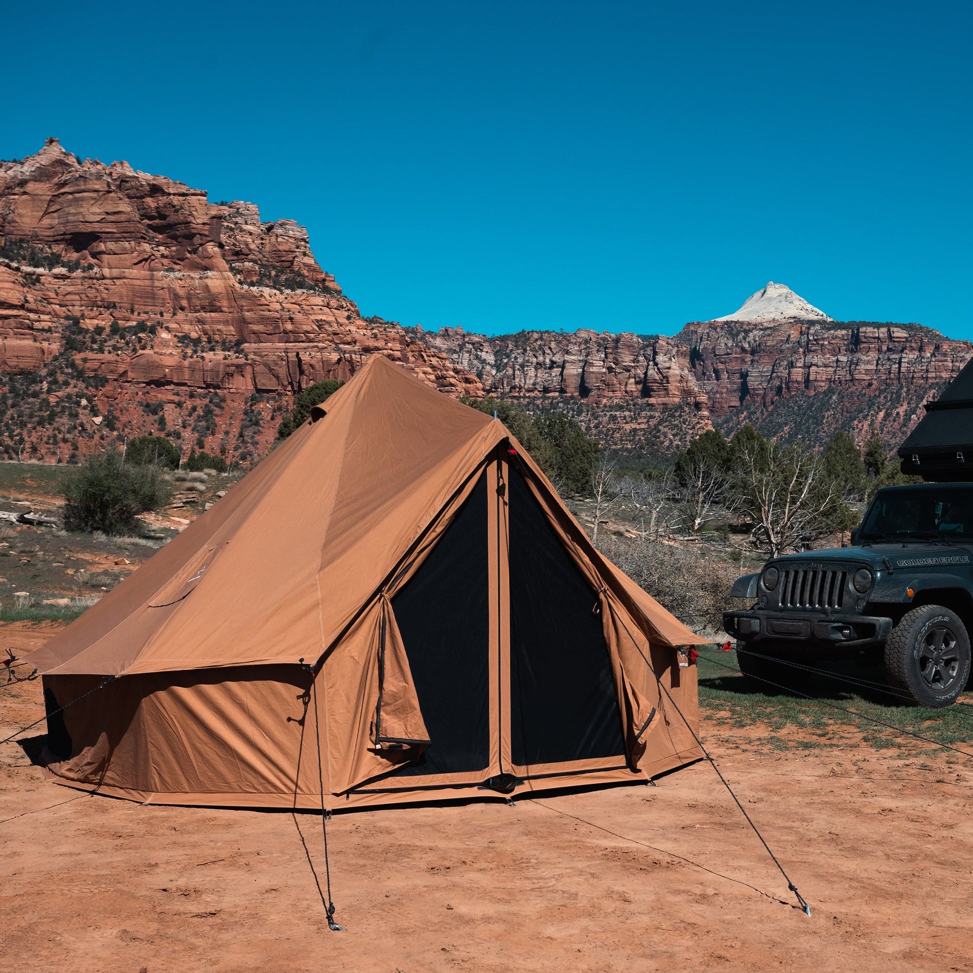 Brown tent set up in a desert landscape with mountains in the background