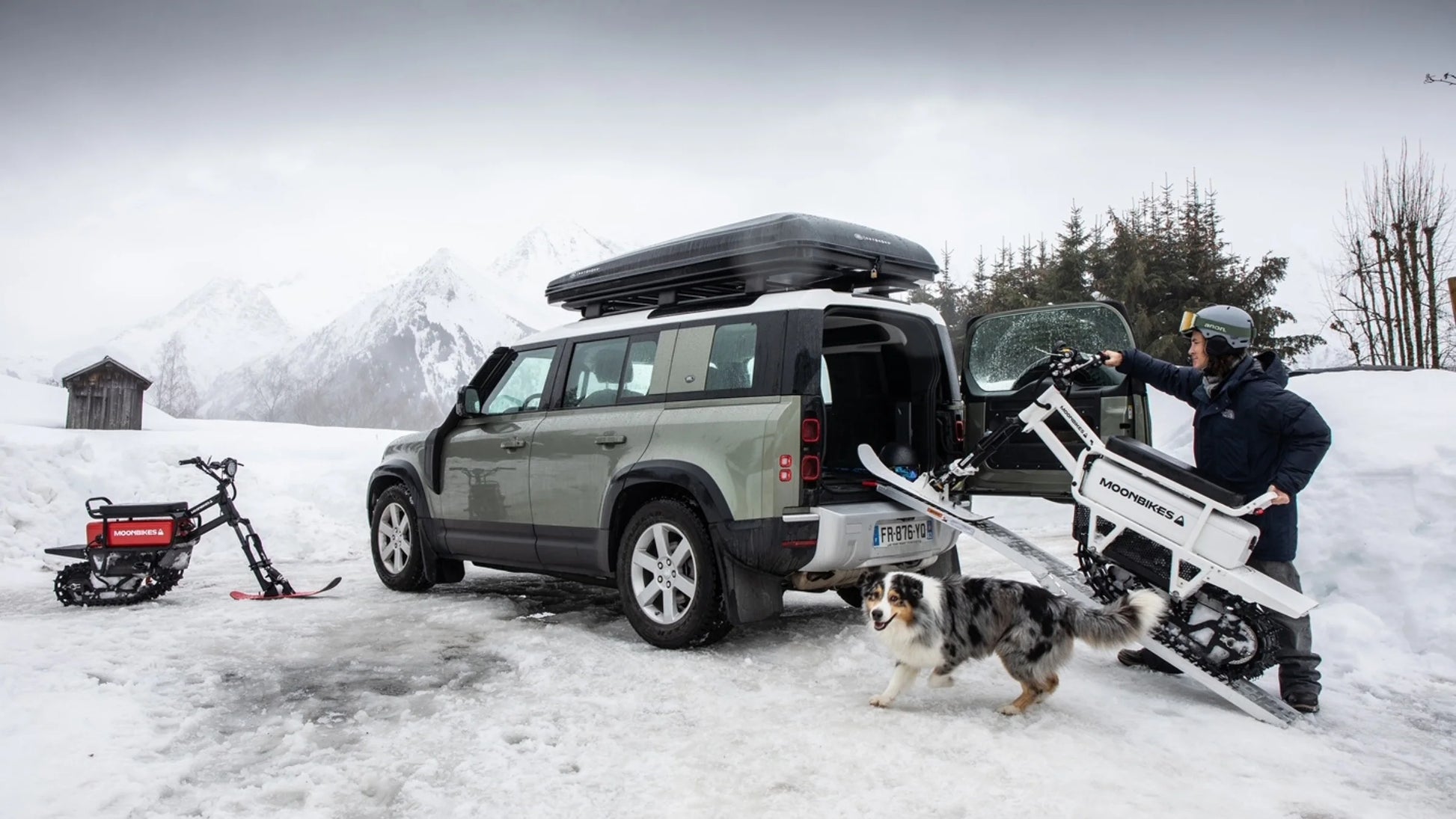 Person loading a snowmobile onto a vehicle in a snowy landscape