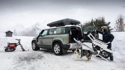 Person loading a snowmobile onto a vehicle in a snowy landscape