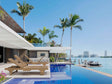 Luxury pool area with lounge chairs, palm trees, and waterfront view.