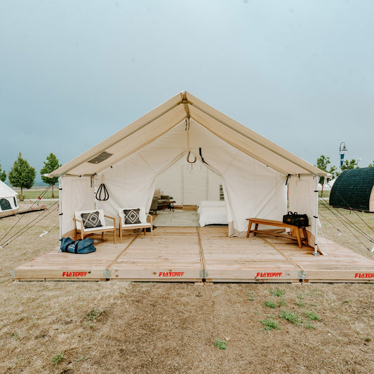 Large beige tent with wooden platform and furniture in a camping setting