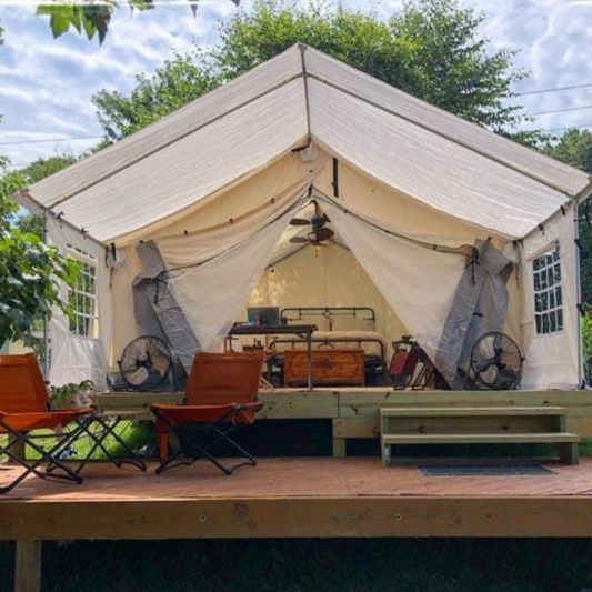 Large beige tent with interior furniture and decor, set outdoors with trees and sky in the background.