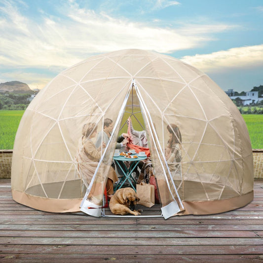 A large beige outdoor igloo garden greenhouse dome tent with a transparent TPU surface. It is set up on a wooden deck with plants inside and a dog lying on the floor.