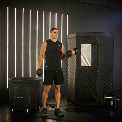 Man holding dumbbells in front of a black sauna box with illuminated vertical lights on the wall.