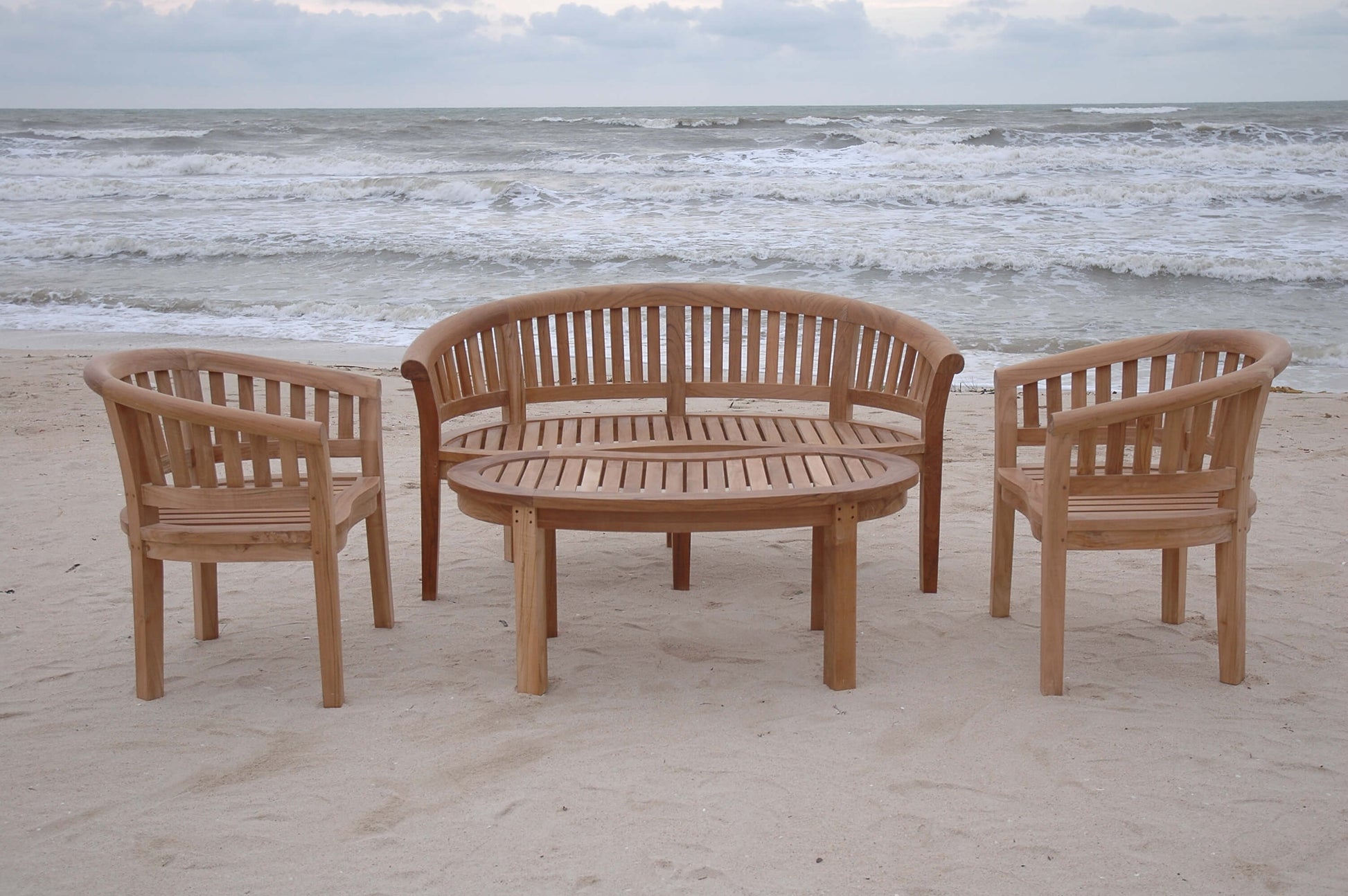 Wooden outdoor furniture set on a sandy beach with ocean waves in the background